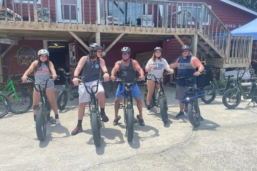 A group of people on bicycles in front of a building with a wooden deck and stairs. 3