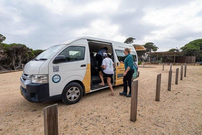 A white van with a yellow stripe parked on a gravel surface, with people boarding and alighting. 2