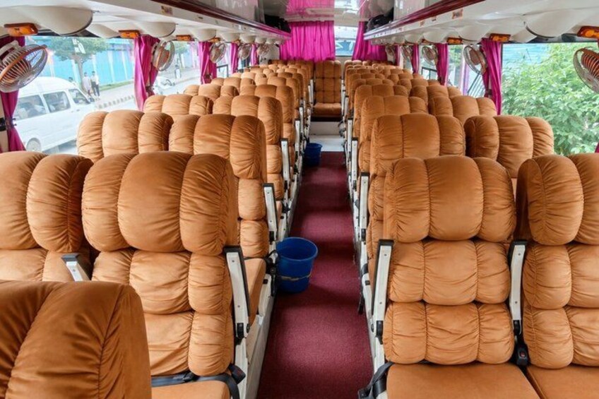 A train interior with rows of orange cushioned seats, a blue bucket, and pink curtains. 1