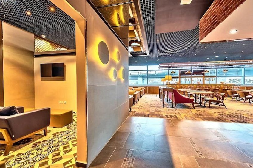 A modern interior with a mix of seating areas, a patterned floor, and a large window overlooking a bar area. 1