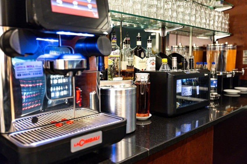 A coffee machine, a glass display case with bottles, and a counter with various items. 3