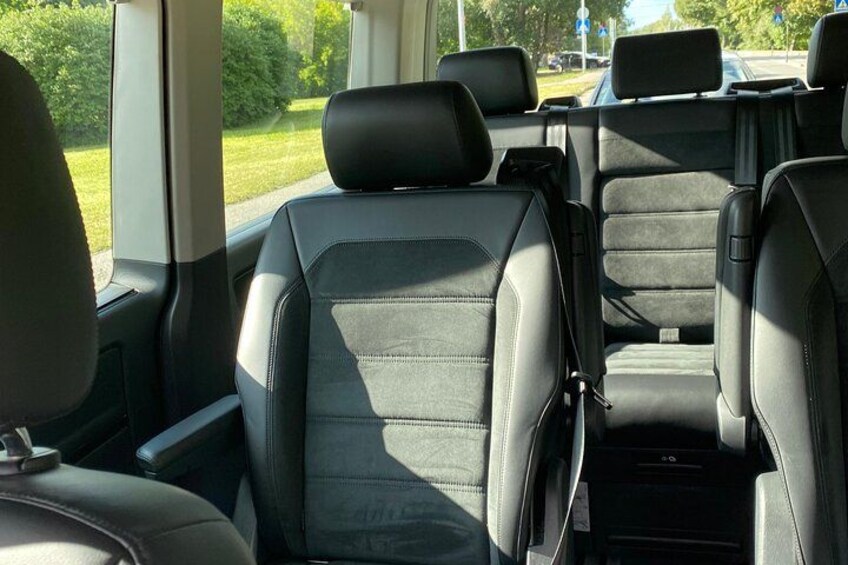 The interior of a vehicle with black leather seats, a center console, and a view of the outside through the windows. 2