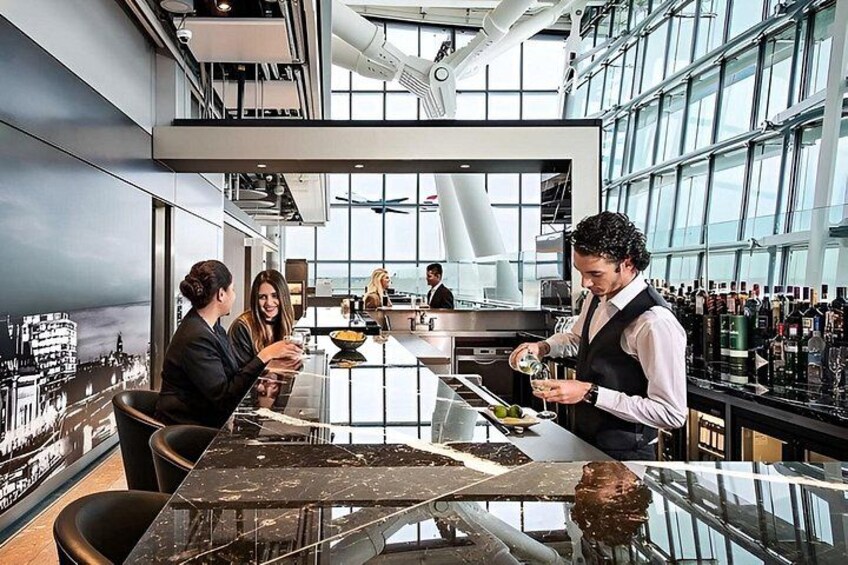 A modern bar with a bartender preparing drinks, a cityscape mural on the wall, and a large window allowing natural light. 1