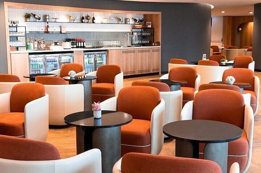 A modern bar area with orange and white chairs, black tables, and a bar counter with various bottles and glasses. 2