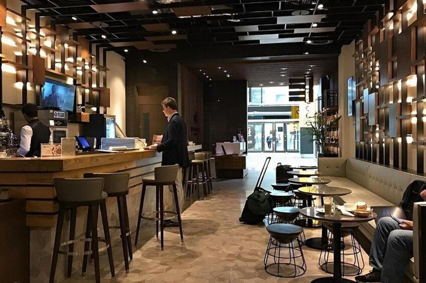 A modern bar with wooden counters, bar stools, and a seating area with round tables and chairs. 4