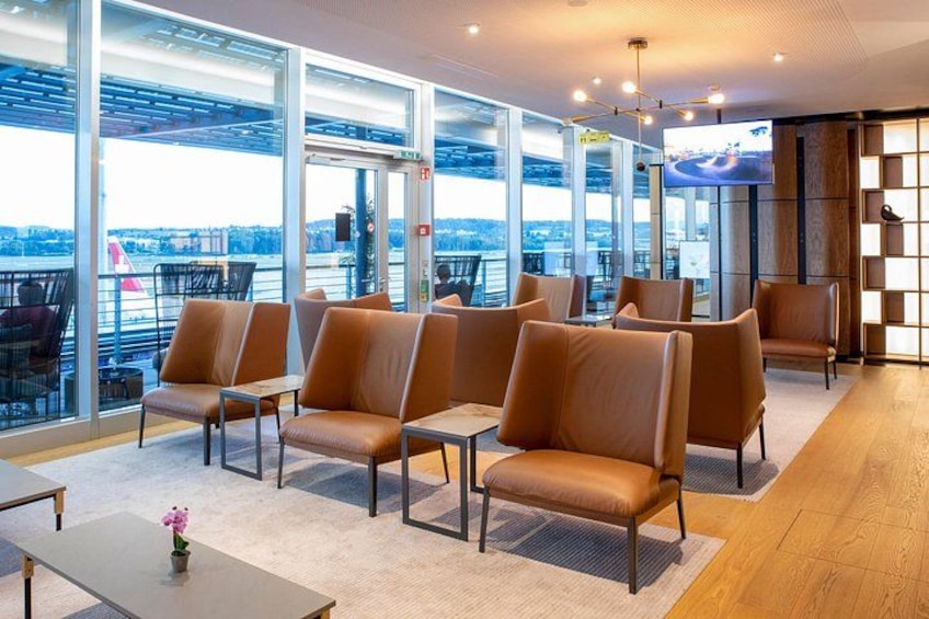 A modern lounge with leather chairs and tables, large windows, and a view of the city. 1