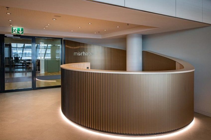 A modern reception desk with vertical wood paneling and a circular shape, situated in a spacious, well-lit lobby area. 2