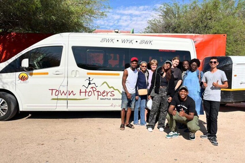 A group of people posing in front of a shuttle bus with the text 'Town Hoppers' and 'Shuttle Service' on it. 3