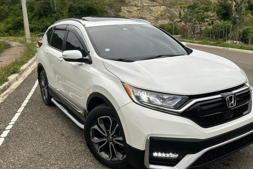 A white Honda SUV parked on a road with a hilly landscape in the background. 1
