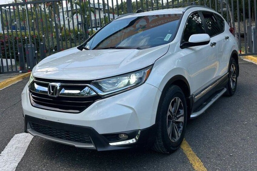 A white Honda SUV parked on a street with a metal fence and greenery in the background. 5