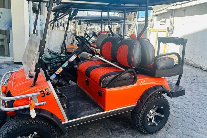 A red golf cart with black and red seats parked on a cobblestone street. 3