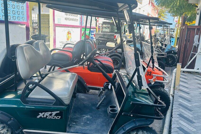A row of golf carts parked on a paved surface. 2