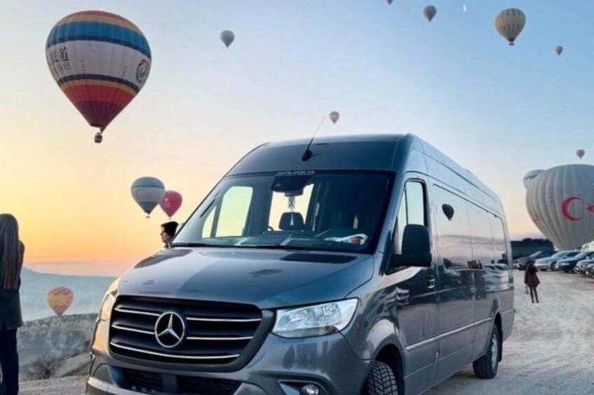 A Mercedes van parked on a beach with hot air balloons in the background. 3