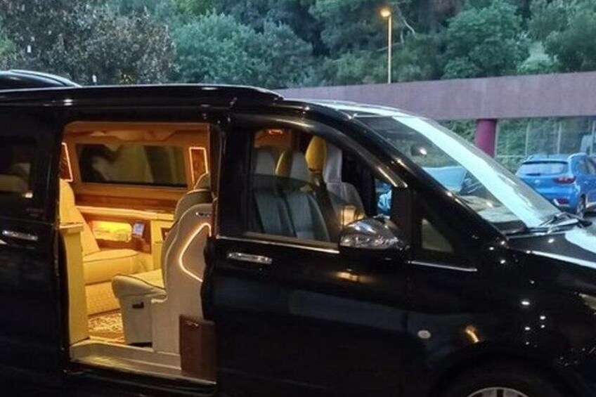 A black van with its door open, revealing a cozy interior with a bed and a small table. 1