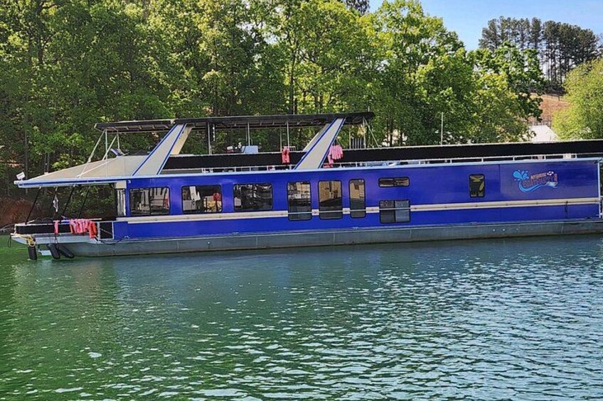 A blue riverboat with a covered deck and windows, floating on calm water. 3
