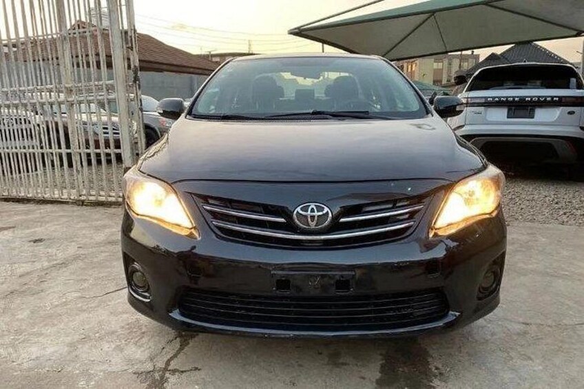 A black Toyota car parked in a lot with a metal fence and other vehicles in the background. 1