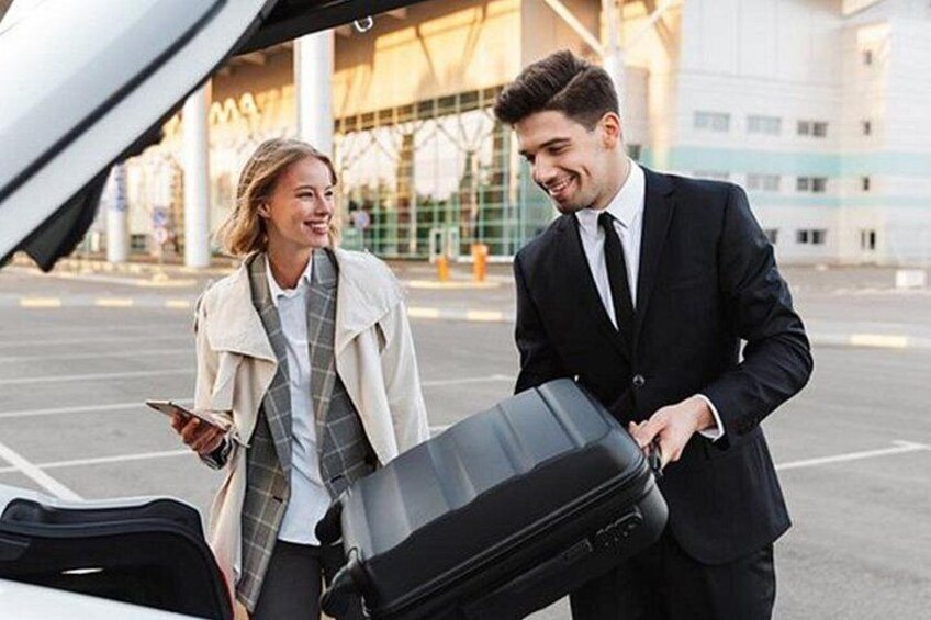 Two people standing next to a car with an open trunk, one holding a suitcase. 3