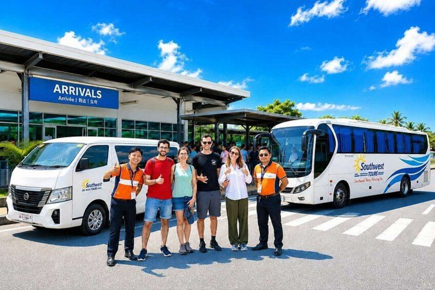 A group of people in front of a bus and a building with an 'Arrivals' sign. 1