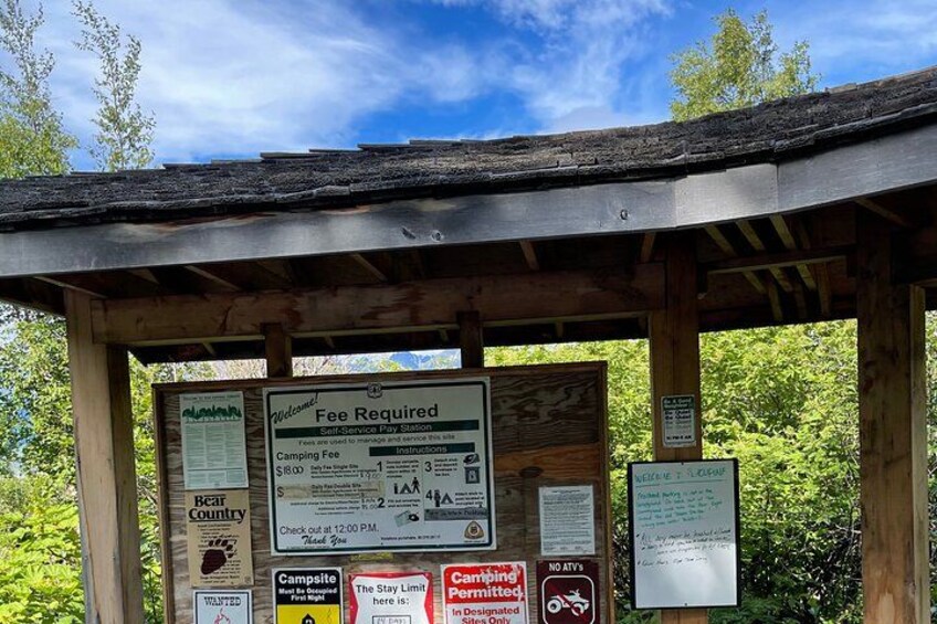 A wooden structure with multiple signs, including a fee required notice and camping information. 3