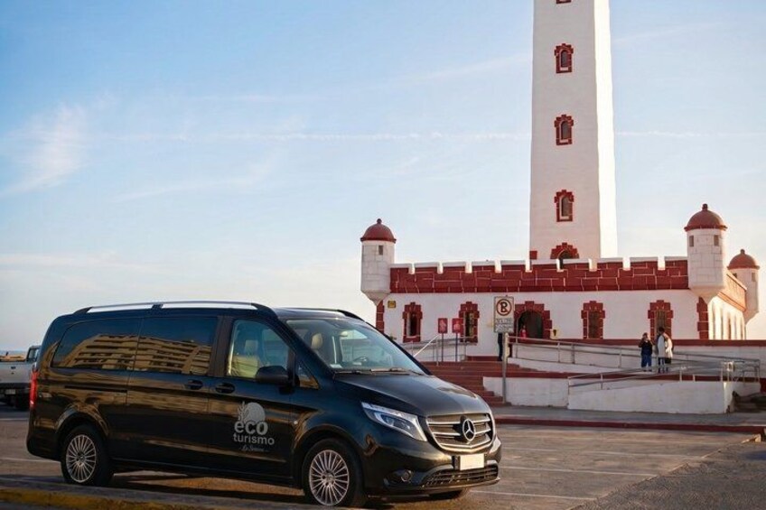 A black van parked in front of a white building with a tall tower and red accents. 3