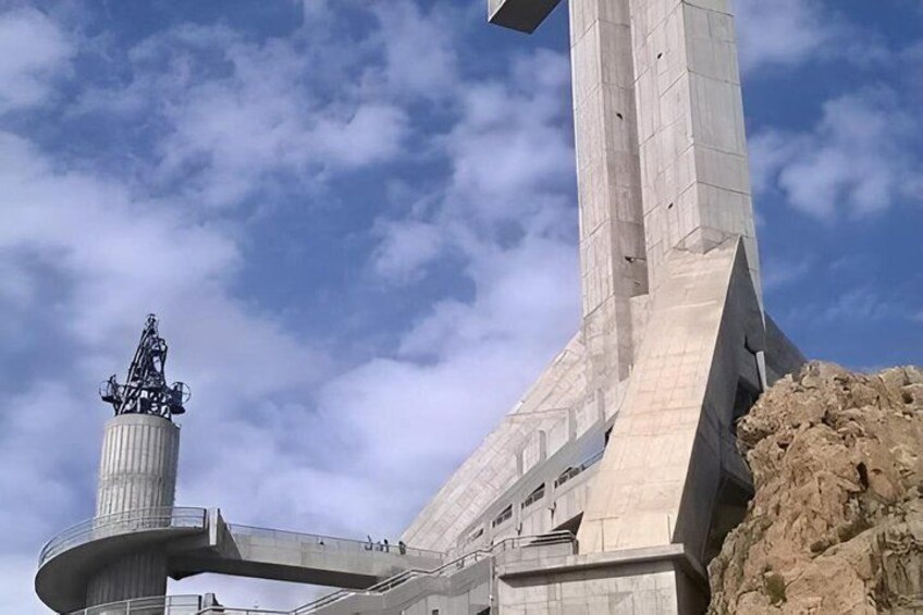A large concrete monument with a statue on top, a curved walkway, and a rocky outcrop. 5