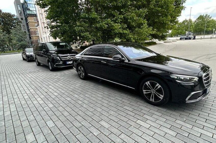 A black car parked on a paved surface with trees and buildings in the background. 1