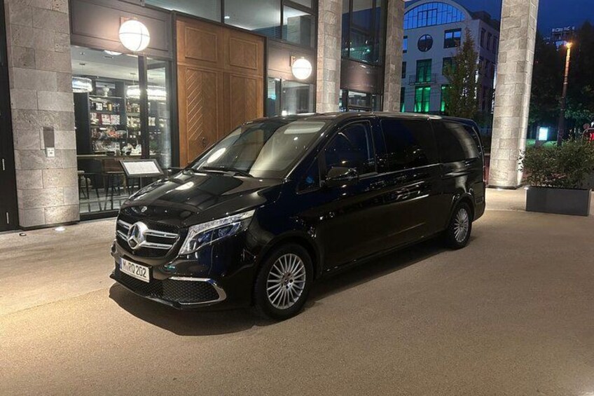 A black Mercedes-Benz van parked in front of a building with large columns and a lit sign. 5
