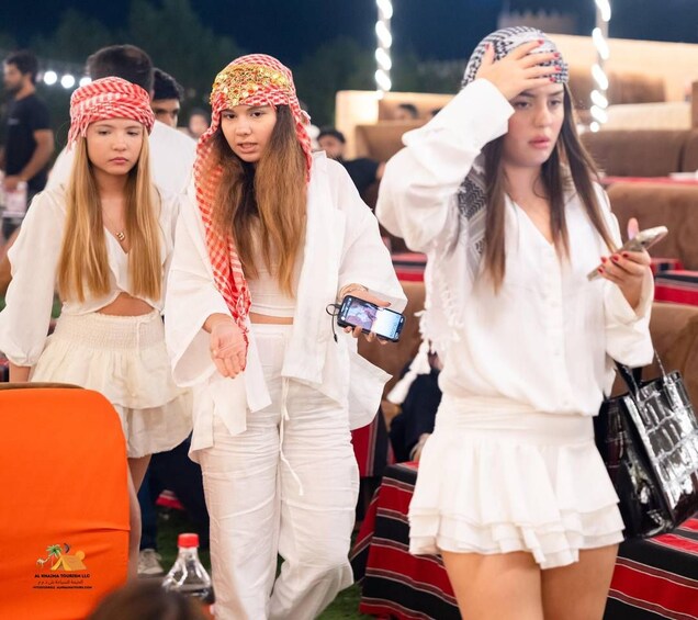Three people walking outdoors at night, dressed in white, with one holding a smartphone. 4
