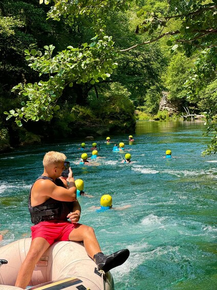 People in a river rafting activity, wearing helmets and life jackets, surrounded by lush greenery. 2