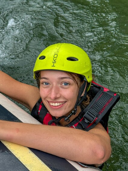 A person wearing a yellow helmet and a life jacket, leaning on a kayak. 5
