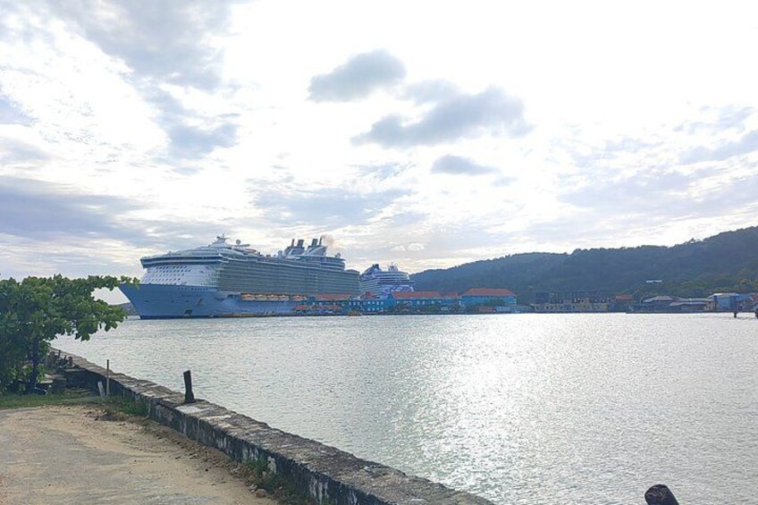 A large cruise ship docked at a port with a calm sea and a hilly landscape in the background. 2