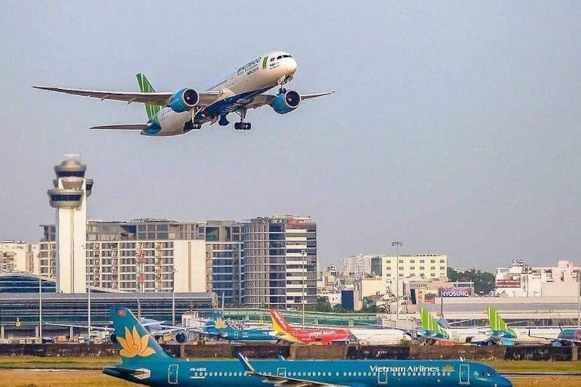An airplane taking off from an airport with buildings and other aircraft in the background. 1