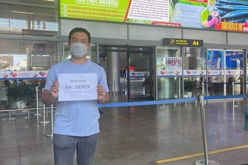 A man holding a sign that reads 'Welcome Mr. DEREK' in an airport terminal. 3