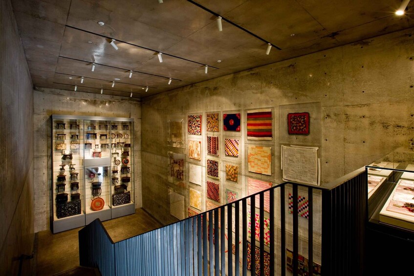 A museum interior with glass display cases and a wall of colorful quilts. 4