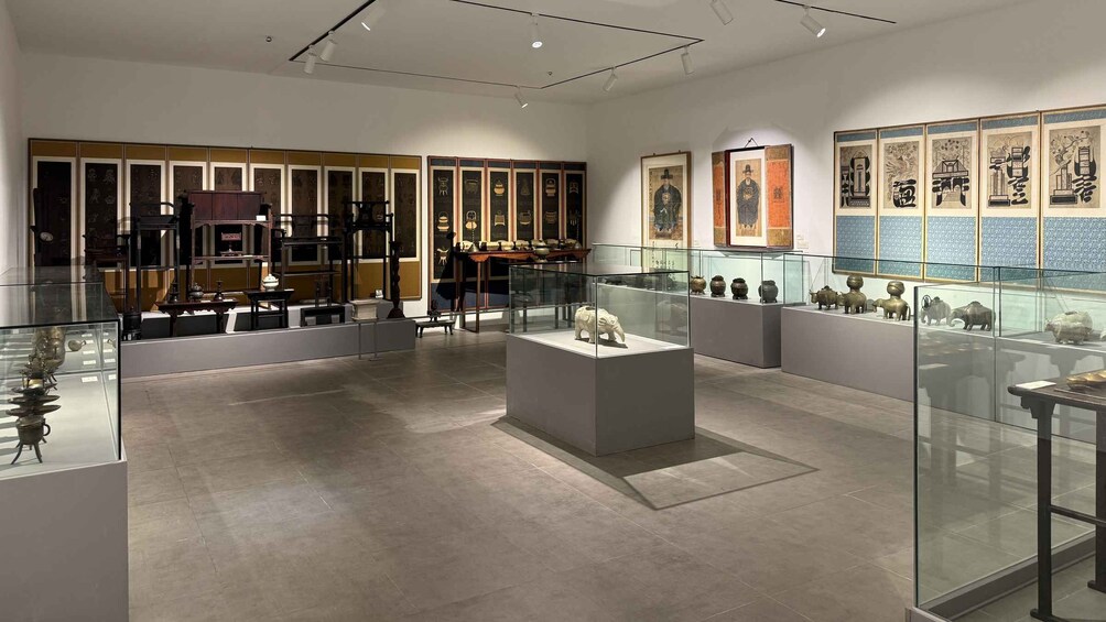 An art gallery with various paintings and sculptures displayed on walls and in glass cases. 2