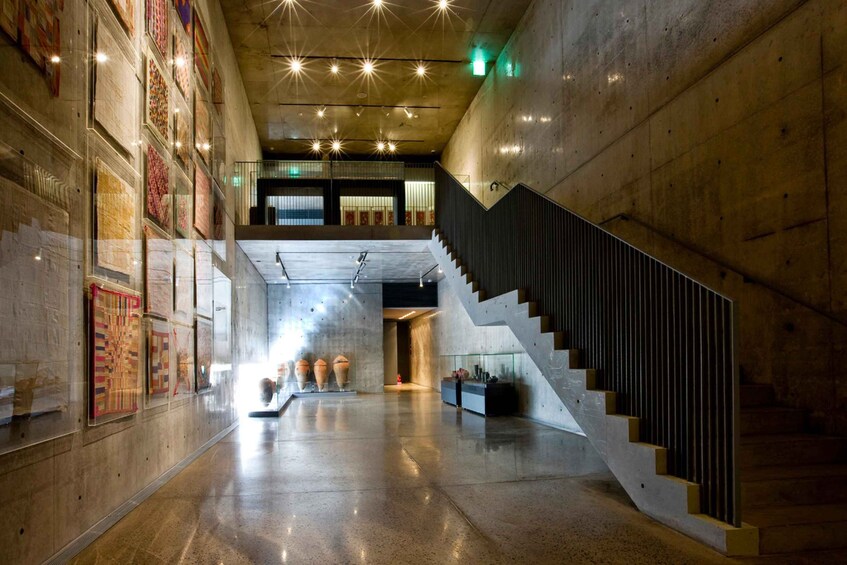 A spacious interior with a staircase, a glass display case with pottery, and artwork on the walls. 3