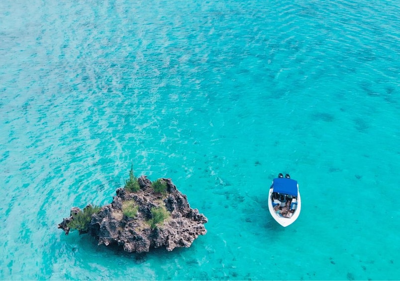 A small rocky island surrounded by turquoise water with a boat anchored nearby. 4