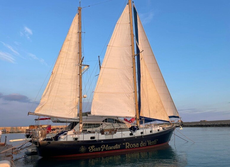 Ein Segelboot namens 'Sua Maestra Rosa dei Venti' liegt in einer Marina festgemacht. 1