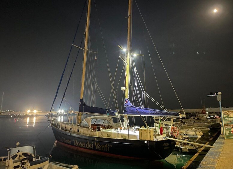 Eine Segelyacht namens 'Rosa dei Venti' liegt nachts in einer Marina vor Anker. 5