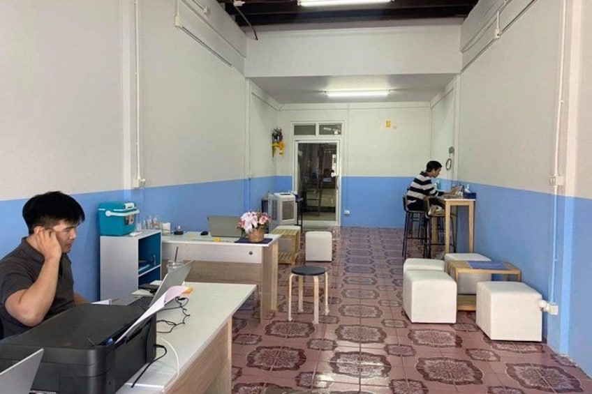 A hallway with two people sitting at desks, one on the left and one on the right. There are chairs, tables, and a patterned floor. 2