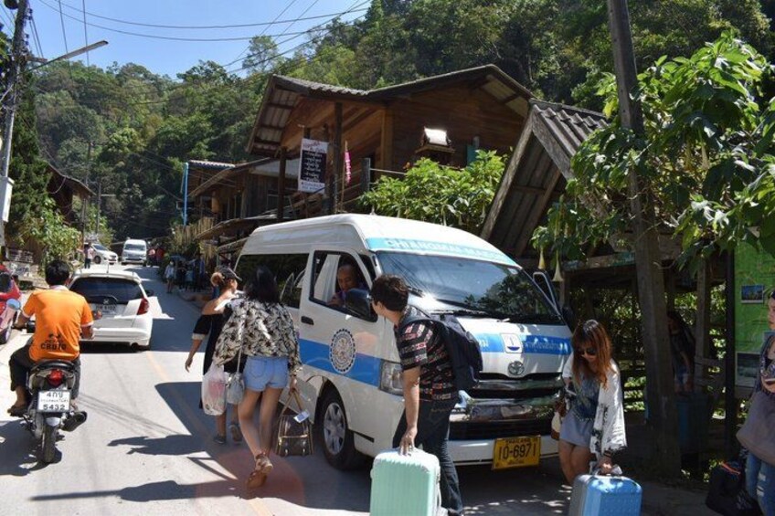 A street with a white van, people with luggage, and a motorbike. 5