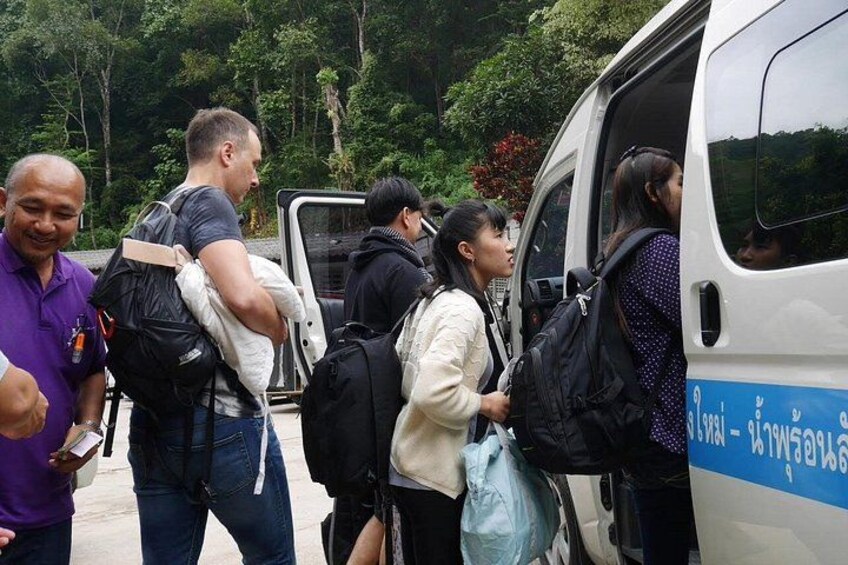 People boarding a white van with blue text, surrounded by greenery. 4