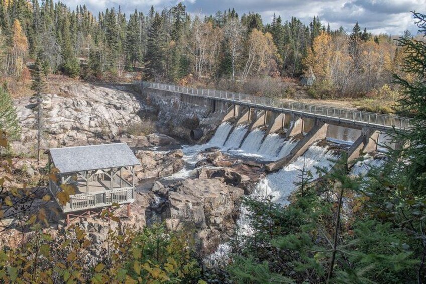 A dam with water flow, a wooden structure, and a forested area. 5