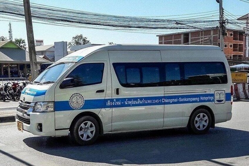 A white van with blue stripes and text, parked on a street with buildings and power lines in the background. 1