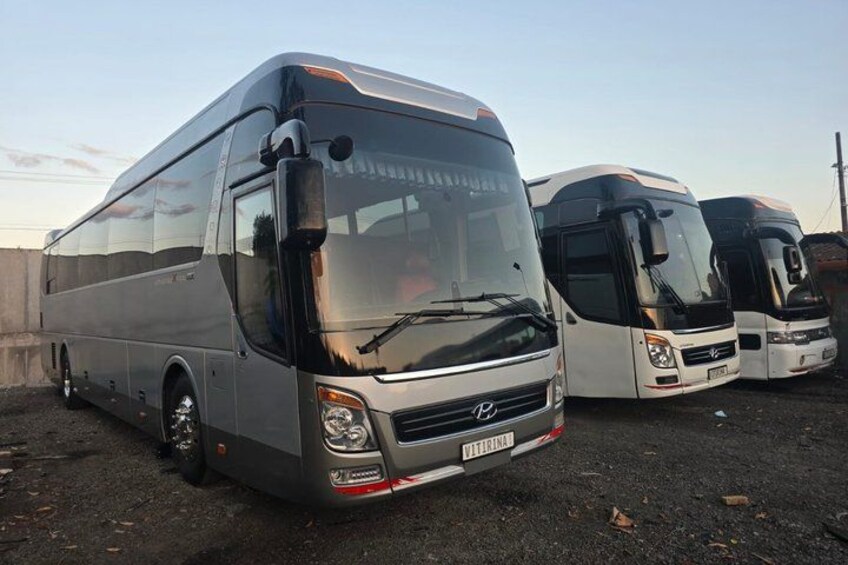 A row of buses parked on a gravel surface. 2