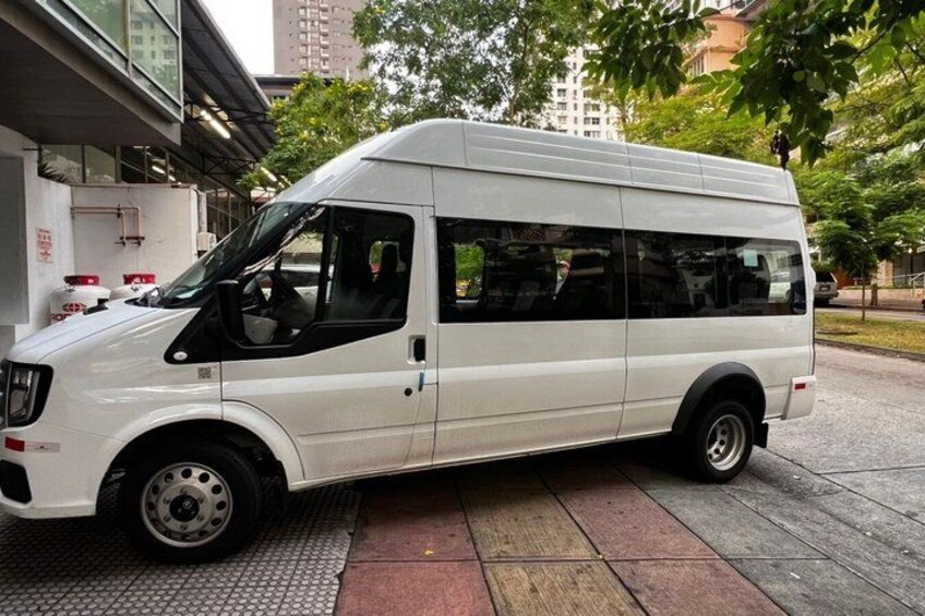 A white van parked on a sidewalk with trees and buildings in the background. 1
