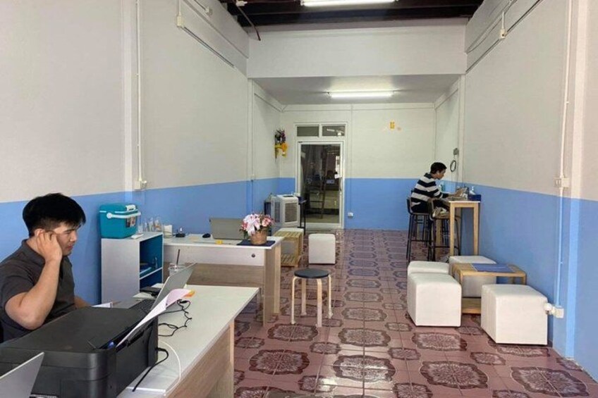 A hallway with two people sitting at desks, one on the left and one on the right. There are chairs, tables, and a patterned floor. 2