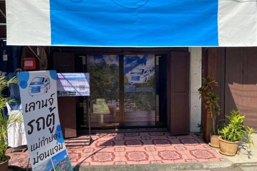 A building entrance with a blue awning, a signboard, and potted plants. 3