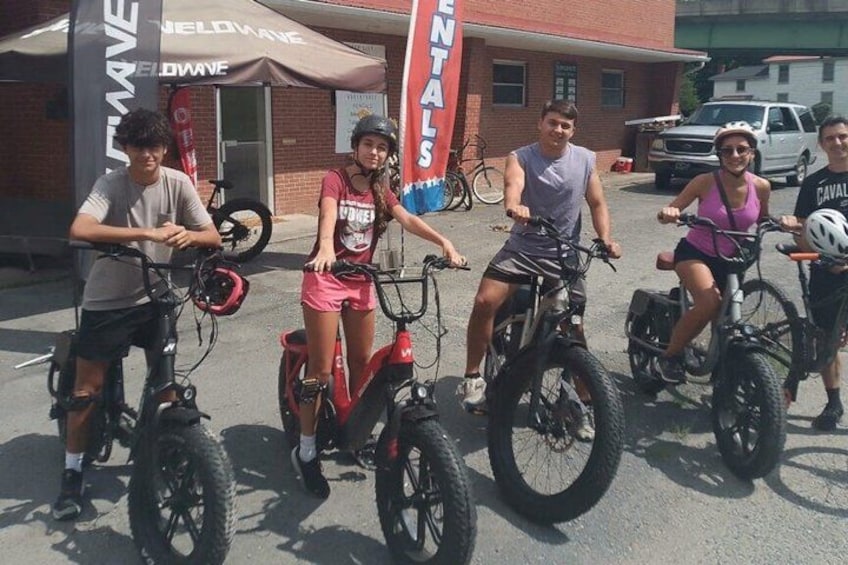 Four people on bicycles in front of a building with a sign that reads 'RENTALS'. 1