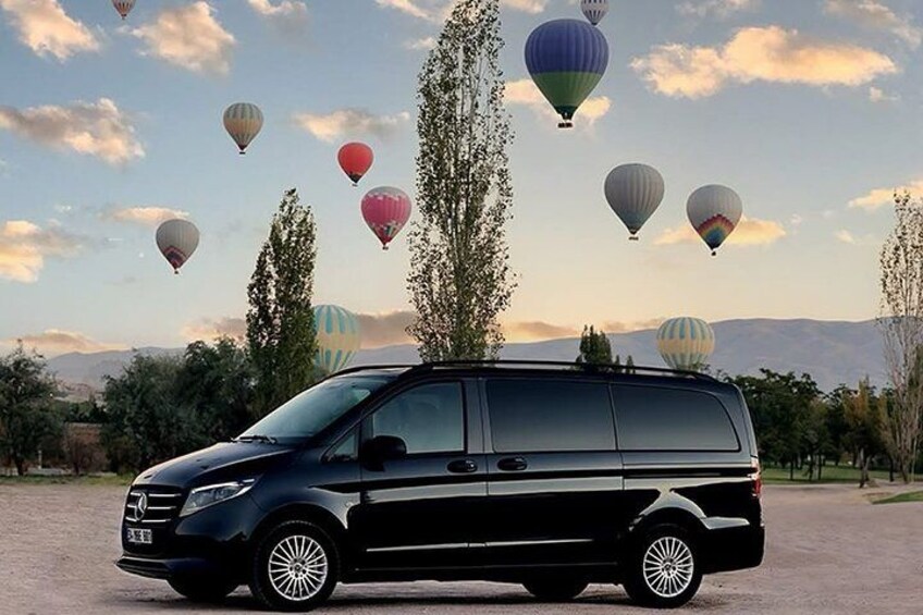 A black minivan parked on a dirt road with colorful hot air balloons in the background. 1
